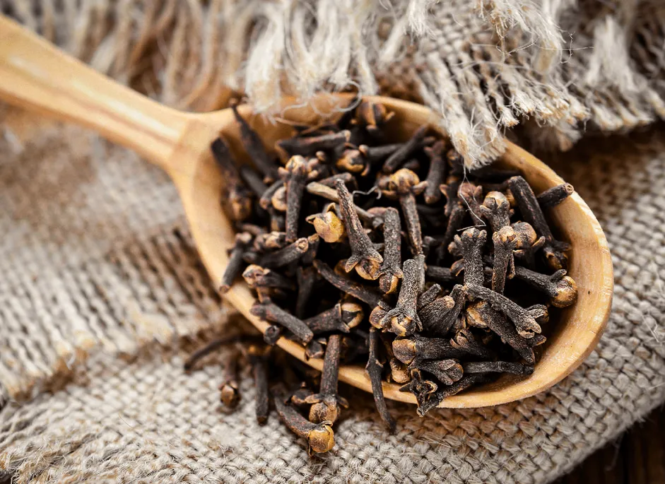 Whole dried clove buds on a wooden spoon resting on hessian