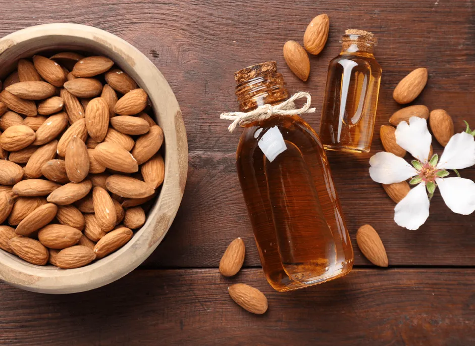 Almonds in a wooden bowl beside two bottles of sweet almond oil
